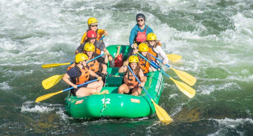 a group of outward bound students wearing helmets and life jackets paddle a raft through whitewater
